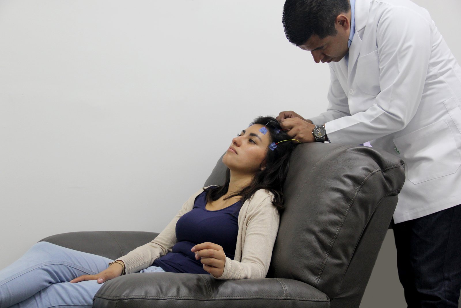 A clinician placing EEG electrodes on a patient reclining in a treatment chair