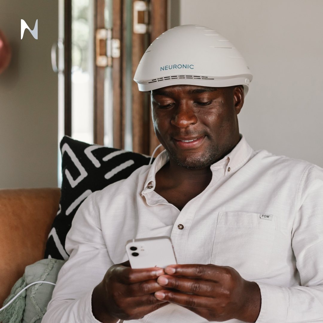 A man wearing a photobiomodulation light helmet while reading on his phone